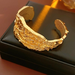 Dettaglio di un bracciale a fascia dorato con texture lava su portagioie in pelle