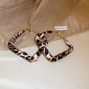 Detail of leopard print fabric geometric earrings with golden hooks and a blooming tag