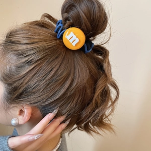 Détail de l'élastique à cheveux bleu en tissu avec breloque 'm' jaune sur un chignon