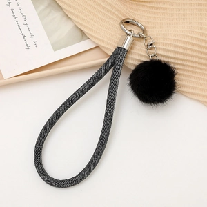 Détail d'une lanière tressée grise et d'un pompon en fourrure noire sur porte-clé