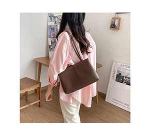 Deep brown leather tote bag worn over shoulder with elegant professional commuter style