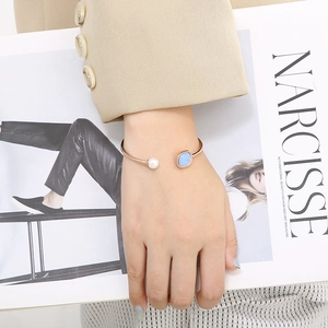 Detailed shot of a gold cuff bracelet featuring a round pearl and a blue rectangular stone