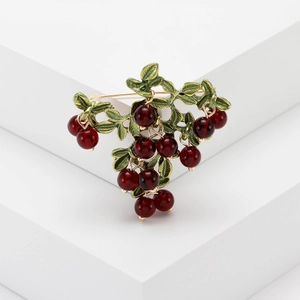 Detail of red cranberry brooch with green enamel leaves and gold-tone metal stem