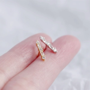 Macro shot of gold and silver bar stud earrings with clear zircon stones on a finger