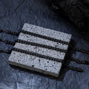 Detailed close-up of matte black Cuban chain necklaces on a textured stone display