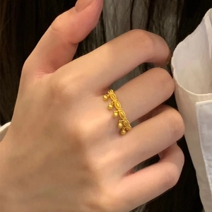 Elegant gold ring featuring bead tassel charms and leaf pendants on a finger