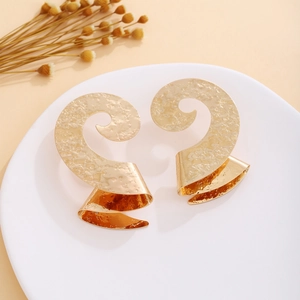 Macro shot of large golden spiral earrings with textured hammered finish on a white stand