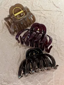 Three acrylic striped claw clips in amber, burgundy, and black on textured paper