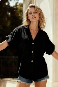 Dettaglio di camicia nera a maniche corte con bottoni e pantaloncini di jeans blu al sole