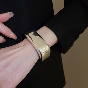 Macro detail of high-polish wavy wide metal cuff bracelet worn on a female wrist