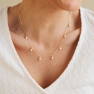 Close-up of elegant gold chain necklace with small pearls worn by a model in V-neck top
