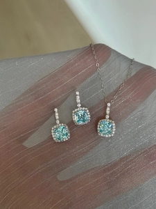 Close-up of light blue halo pendant and earrings set on shimmering fabric