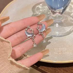 Macro shot of celestial silver drop earrings with blue crescent moon and star details