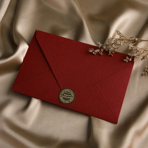 Macro view of burgundy linen-textured envelope with gold seal on luxury silk
