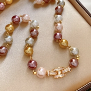 Detailed macro shot of gold H-shaped clasp with zircons on a multicolor pearl necklace