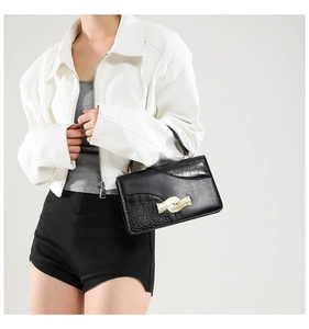 Detail of black square handbag featuring gold wave buckle and crocodile texture
