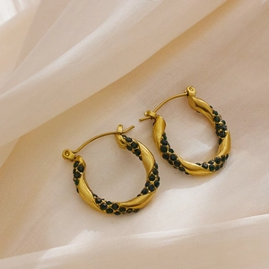 Detail of gold twisted hoop earrings featuring dark green gemstones on silk fabric