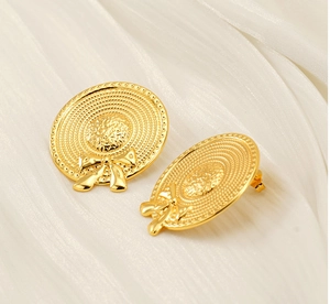 Detailed close-up of golden bow straw hat earrings with fine woven metal texture