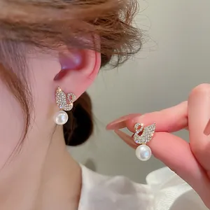 Macro shot of gold swan earrings featuring crystal pavé and round white pearls