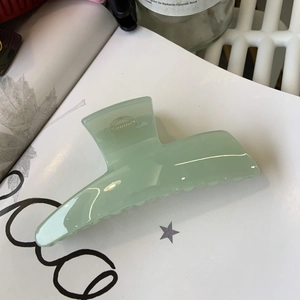Elegant mint green large hair claw clip in a glossy finish on a minimalist book