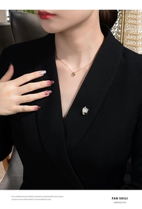 Close-up of a white cat opal brooch and geometric gold necklace on a black blazer
