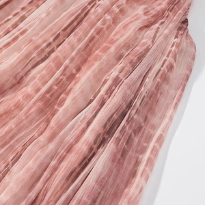 Dettaglio del tessuto in chiffon plissettato tie-dye rosa con trame verticali morbide
