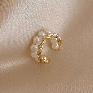 Dettaglio di un ear cuff a doppio strato intrecciato in oro con piccole perle bianche
