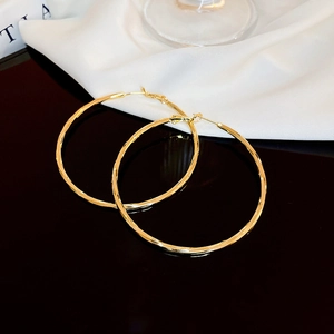 Detail of gold-plated hollow hoop earrings featuring textured faceted metal surfaces