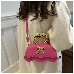 Pink crossbody bag featuring a wavy bottom profile and gold bow-tie metal handle detail
