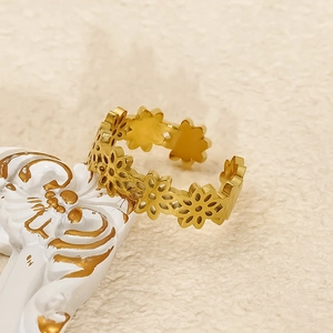 Gold hollow floral smile ring in titanium steel on a luxury textured display stand