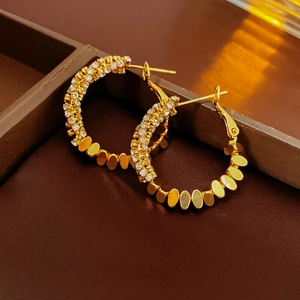 Macro shot of gold hoop earrings with sparkling cubic zirconia and oval metal plate detail