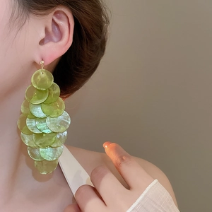 Detail of long pale green shell disk tassel earrings with gold metal stud on model
