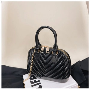 Detail of glossy black patent leather shell bag with elegant gold chain strap