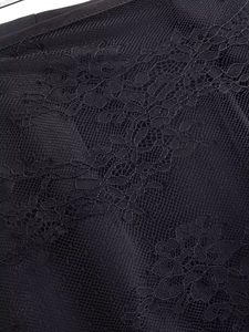Close-up of black floral lace texture on satin trousers showing intricate mesh patterns