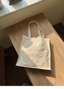 Detail shot of beloved embroidery on beige canvas tote bag with high-quality texture