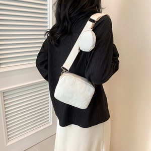 Detail of white camera bag with embossed heart patterns and small round coin purse
