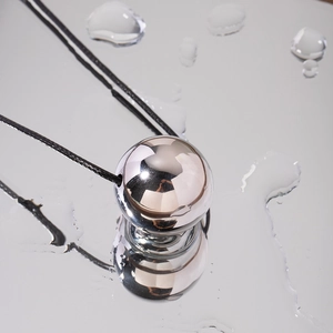 Minimalist silver stainless steel sphere pendant on black waxed cord with water droplet background