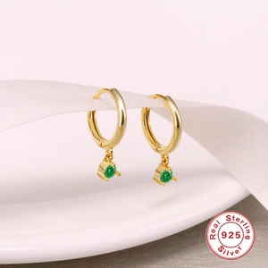 Macro shot of gold S925 sterling silver hoop earrings with dangling green zircon stones