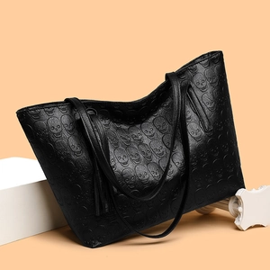 Black leather tote bag with skull relief patterns and tassel on stone podium