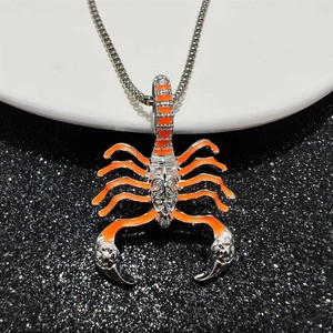 Close-up of silver scorpion pendant with orange enamel details on a metal chain