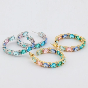 Macro detail of gold and silver hoop earrings featuring colorful oval zircon stones