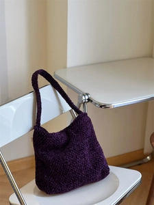 Borsa a spalla hobo in tweed intrecciato viola appesa a una sedia in un caffè minimal