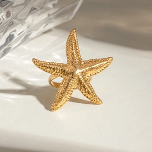 Top view of a gold-tone starfish ring with hammered texture on a light background