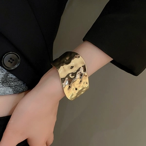 Detail of wide gold cuff bracelet featuring an irregular hammered liquid metal texture