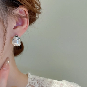 Close-up of irregular baroque pearl earrings with silver edges worn by a female model