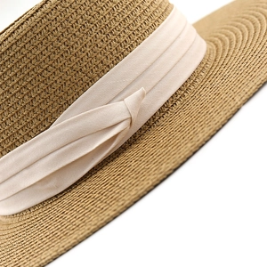 Detail of woven straw sun hat featuring a beige ribbon bow and tight texture