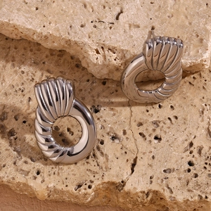 Macro detail of silver geometric earrings with shell texture and twisted ring design
