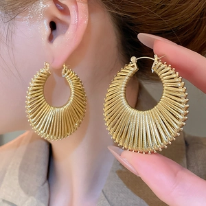 Détail de boucles d'oreilles créoles dorées tissées ajourées au design rayons