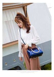 Outdoor street style shot of a glossy royal blue patent leather Boston bag with gold handles