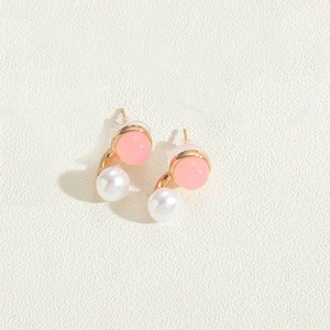 Detail of pink acrylic bead and white pearl stud earrings on textured fabric